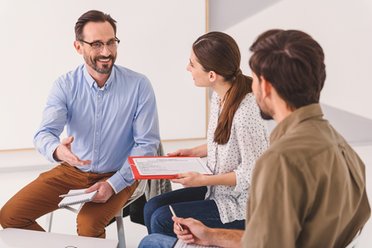 © www.adobestock.com - Yaroslav Astakhov Zwei Männer und eine Frau sitzen zusammen und unterhalten sich