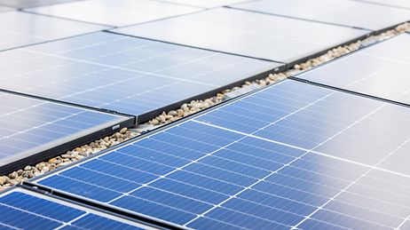 © Mainova Mehrere blaue Solarpaneele auf einem Kiesdach, in Reihen angeordnet, mit gitterförmiger Zellstruktur.