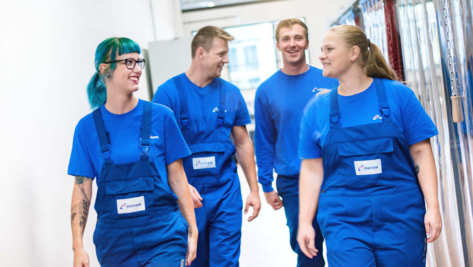© Mainova/AndreFormer Gruppe Auszubildende laufen in Arbeitskleidung einen Gang entlang