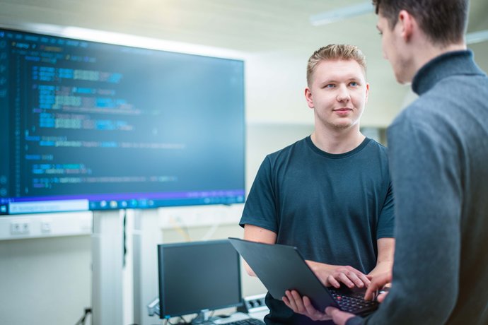 © Mainova/AndreFormer Zwei Auszubildende stehen mit Notebook im Schulungsraum und besprechen sich