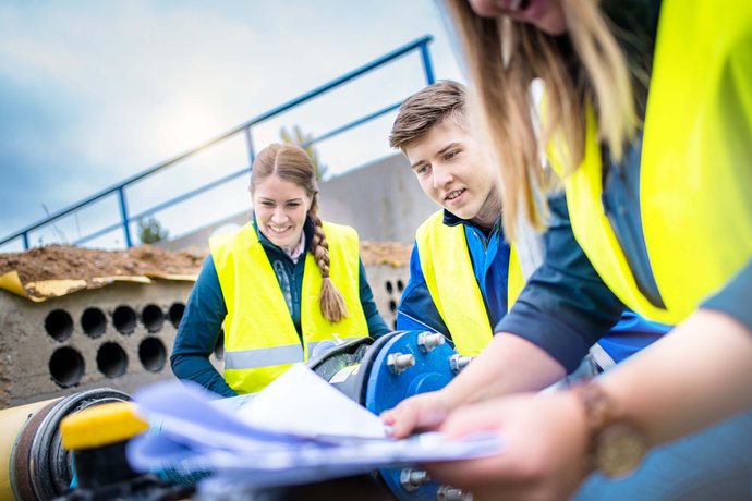 © Mainova/AndreFormer Gruppe Studenten sitzen auf einer Baustelle und betrachten einen Bauplan