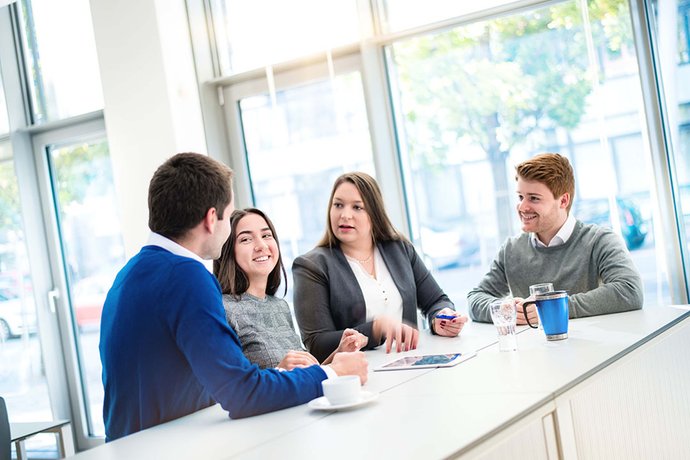 © Mainova/AndreForner Eine Gruppe Studierende stehen am Tisch und sprechen miteinandet