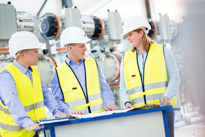 © Mainova/AndreFormer Drei Studierende stehen am Tisch vor einen Plan und besprechen diesen