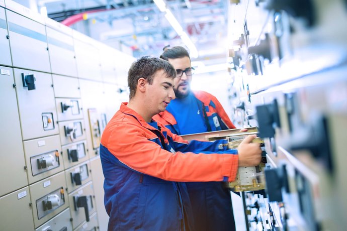 © Mainova/AndreFormer Zwei Techniker vor einer Schaltanlage und tauschen ein Modul aus