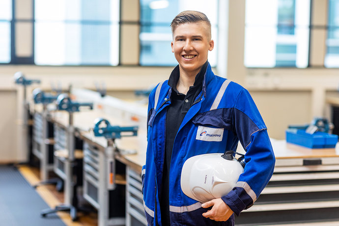 © Mainova/DennisMöbus Nklas Bähring im Blaumann und Helm unter dem Arm vor einer Werkbank des Ausbildungszentrum
