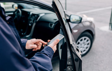 © istock.com/Youngoldman Älterer Mann mit Handy steht vor einem Carsharing-Auto.