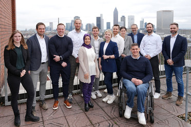 © Mainova Eine Gruppe lächelnder Menschen in Business-Kleidung steht auf einer Terrasse vor Frankfurter Skyline
