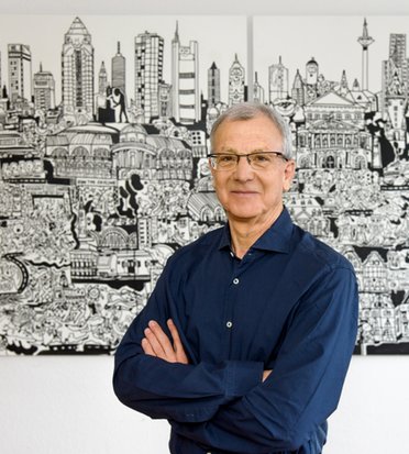 © Bernd Kammerer Jo Schindler vor Wandbild mit Stadtsilhouette, Arme verschränkt.