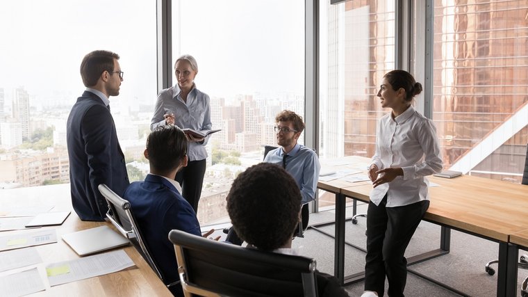 © www.istock.com/fizkes Zwei Frauen und vier Männer sprechen in einem Meetingraum miteinander