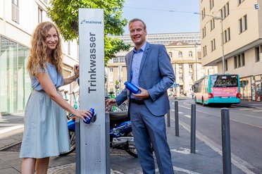 © Mainova AG Eine Frau und ein Mann zapfen Wasser an einem Edelstahl-Trinkbrunnen