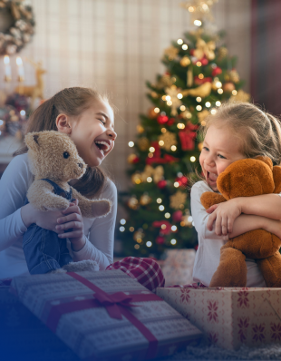Zwei kleine Mädchen spielen und kuscheln mit ihren Teddybären vor einem Weihnachtsbaum