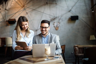 © istockphoto.com/nd3000 Eine Frau und ein Mann beraten sich in einem Café und schauen gemeinsam auf ein Tablet.