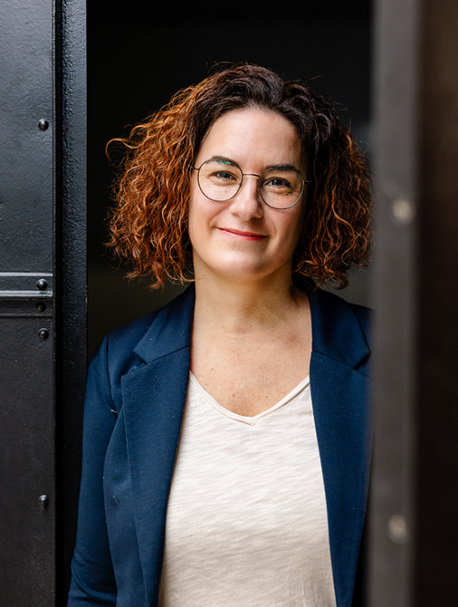 © Stilmanöver/RamonHaindl Frau mit lockigen Haaren, Brille und blauem Blazer lächelt freundlich in die Kamera.