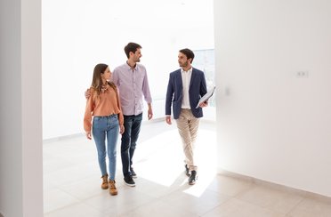 Immobilienmakler führt ein junges Paar durch eine leer stehende Wohnung