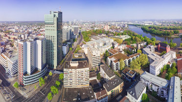 © stock.adobe.com/Igor Link Vogelperspektive einer Stadt zeigt Hochhäuser in verschiedenen Höhen, Straßen, einen Fluß und Bäume.