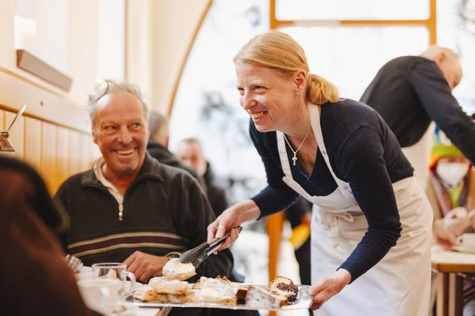 © NoiCrew Eine Frau serviert einem älteren Herren ein Stück Kuchen.