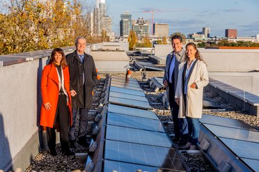 Vier Menschen stehen auf einem Dach mit Photovoltaikanlagen