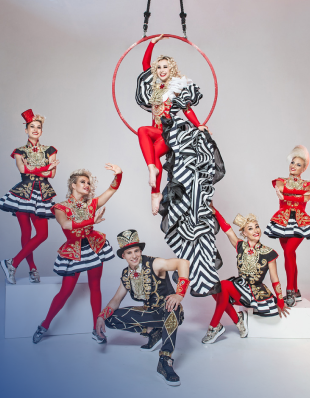 Circus Athleten in weißer Kleidung aufgereiht und oben eine Frau in einem Ring sitzend