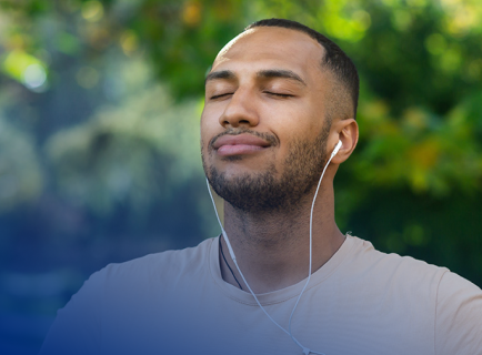 Mann mit Kopfhörern und geschlossenen Augen genießt im Grünen die Musik