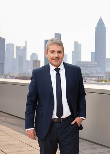 Mann im Anzug mit Krawatte steht auf einer Terrasse vor einer Skyline. Professioneller, formeller Ausdruck.