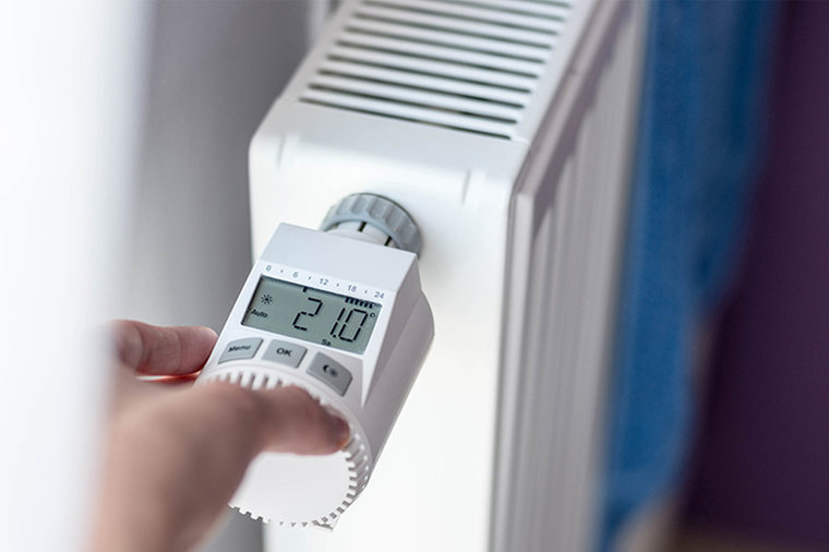 © stock.adobe.com/Daniel Jędzura Hand programmiert ein Thermostatventil an einer Heizung