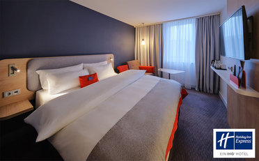 © Hotel Holiday Inn Express Frankfurt Messe Gemachtes Doppelbett wird schräg betrachtet, im Hintergrund sind halb zugezogene Gardinen
