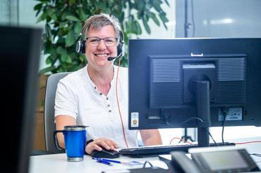 Eine Person mit Kopfhörern sitzt vor einem Computerbildschirm in einem Büro.