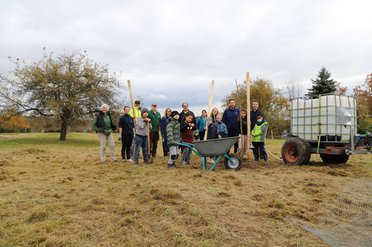 Eine Gruppe von Menschen steht auf einem Feld neben einem Schubkarren und einem Traktor mit Wassertank.