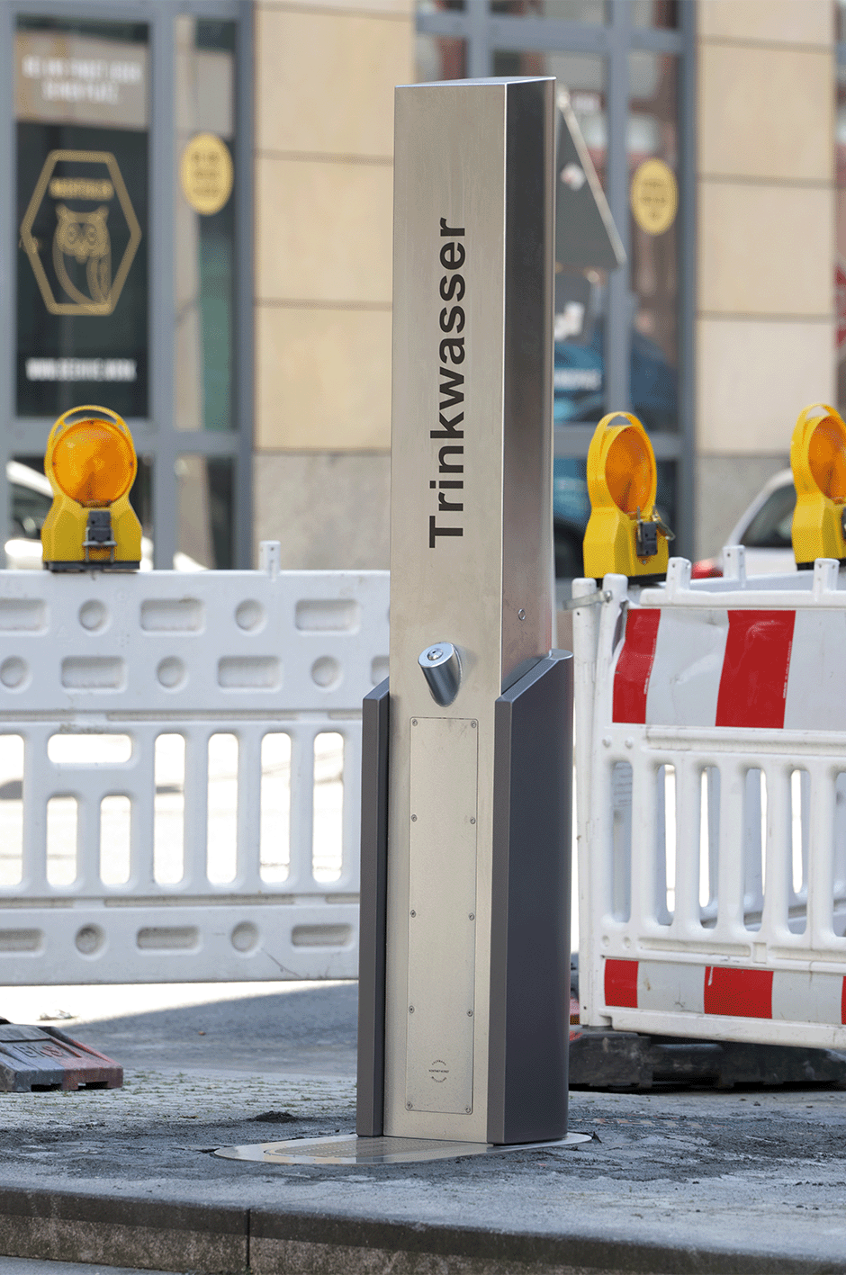 Eine Trinkwasserstation im Freien mit einem Schild "Trinkwasser", umgeben von Absperrungen und Warnleuchten.