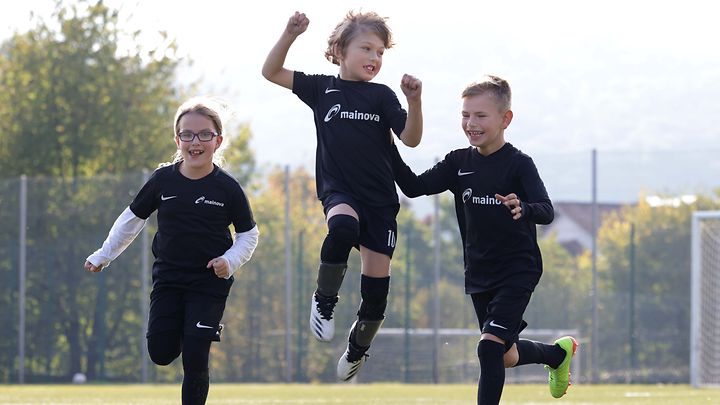 Drei Kinder in Mainova Trikots rennen über ein Fußballplatz