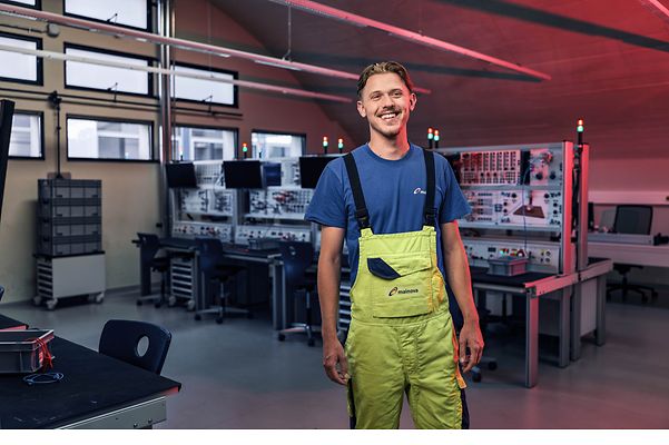 Junger Man steht selbstbewusst in einem Werkraum und lächelt in die Kamera