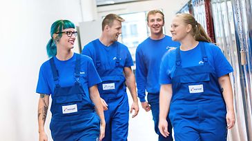 Gruppe Auszubildende laufen in Arbeitskleidung einen Gang entlang