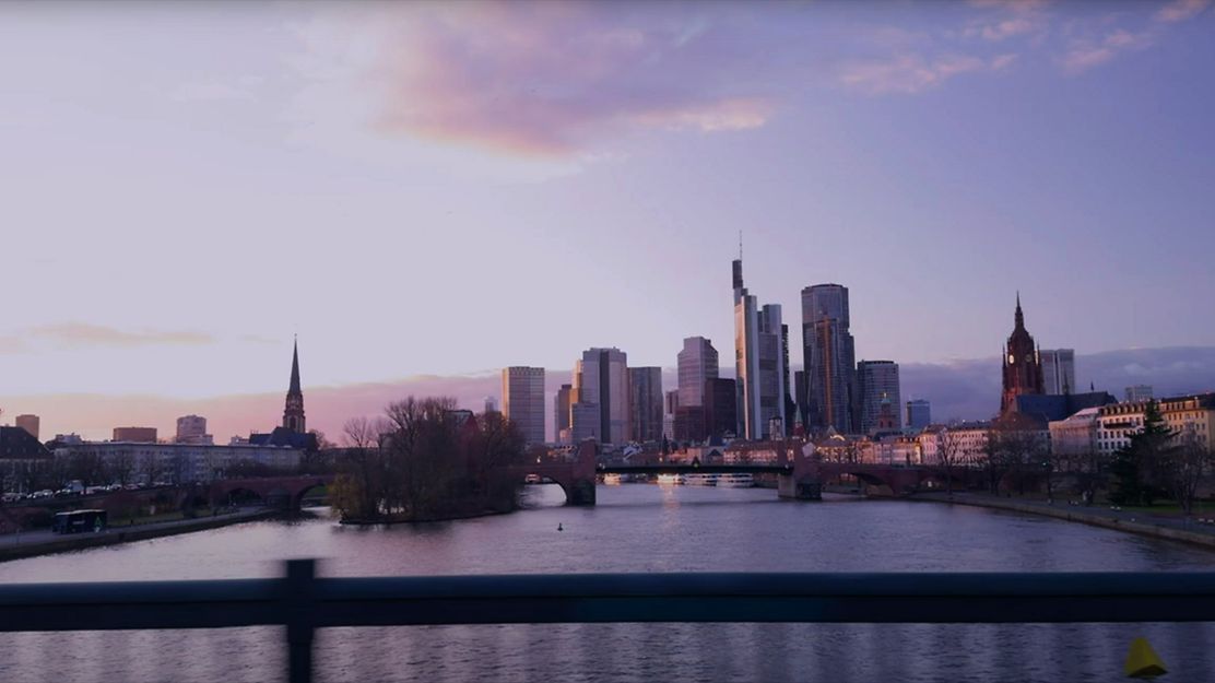 © Mainova Skyline von Frankfurt am Main bei Sonnenuntergang mit Fluss, Brücken und Hochhäusern im Hintergrund.