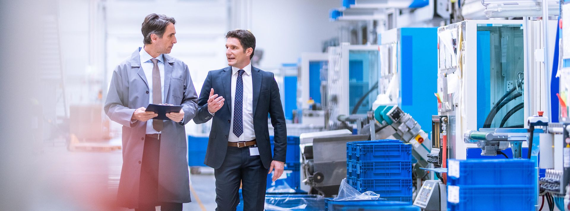 © iStock.com/vm Zwei Geschäftsleute laufen durch Produktionshalle