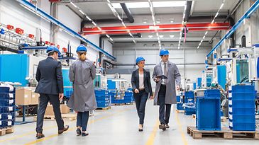 Geschäftsmänner und Geschäftsfrauen laufen durch eine hell beleuchtete Produktionshalle