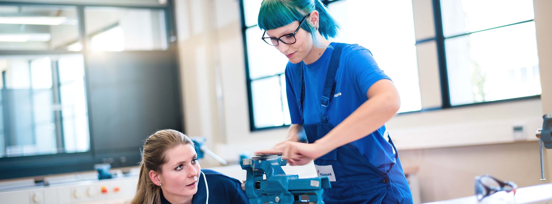 Ausbilderin kontrolliert die Arbeit einer Auszubildenden an einen Schraubstock 