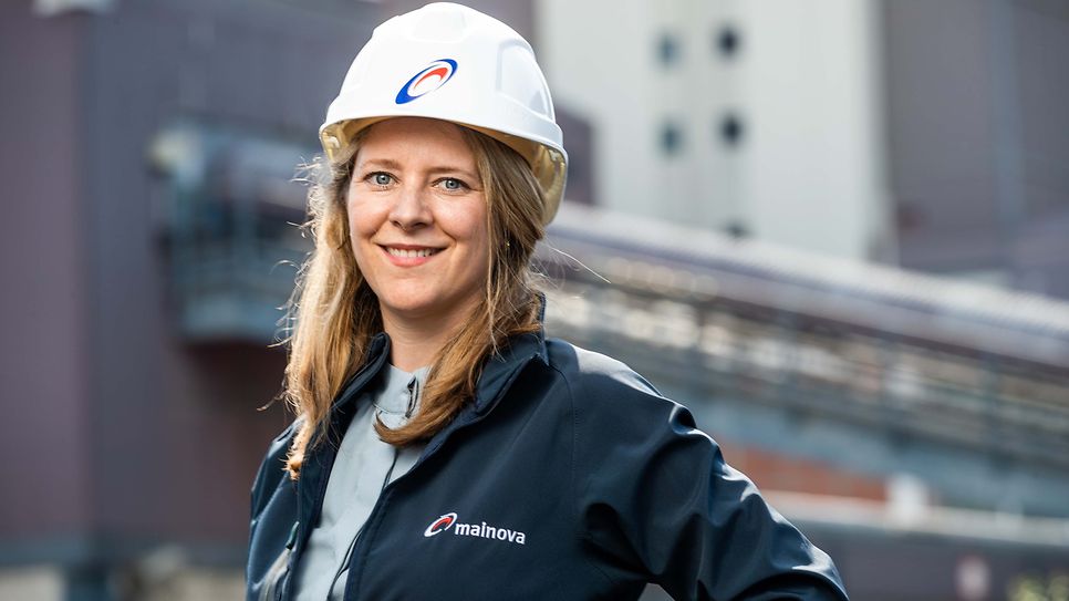 © Mainova/AndreFormer Selina Schad Peter schaut mit Bauhelm in die Kamera. Um Hintergrund verschwommen steht das Mainova Kraftwerk West.