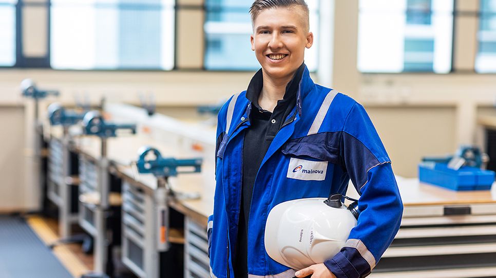 © Mainova/DennisMöbus Nklas Bähring im Blaumann und Helm unter dem Arm vor einer Werkbank des Ausbildungszentrum