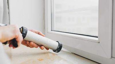 Hände dichten ein Fenster mit Dichtmasse aus einer Spritze ab