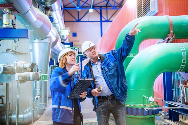 Frau und Mann mit Schutzhelm betrachten Leitungen an der Decke, Und er zeigt auf etwas außerhalb des Bildes