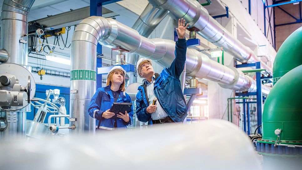 © Mainova/AndreFormer Frau und Mann mit Schutzhelm betrachten Leitungen an der Decke