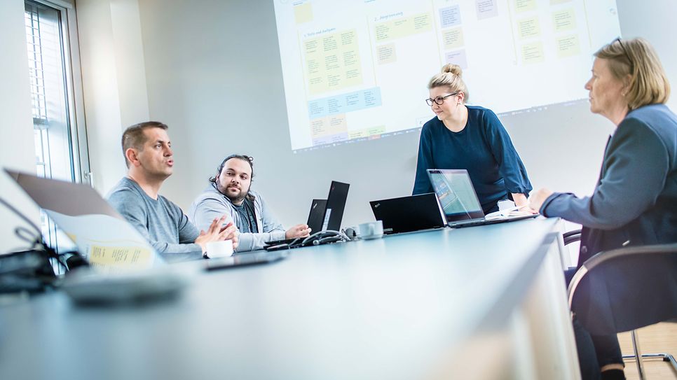 © Mainova/AndreFormer Gruppe sitzt am Konferenztisch und es wird über eine Beamerfolie gesprochen