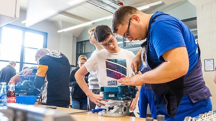 Schüler steht an Werkbank und schaut beim feilen zu