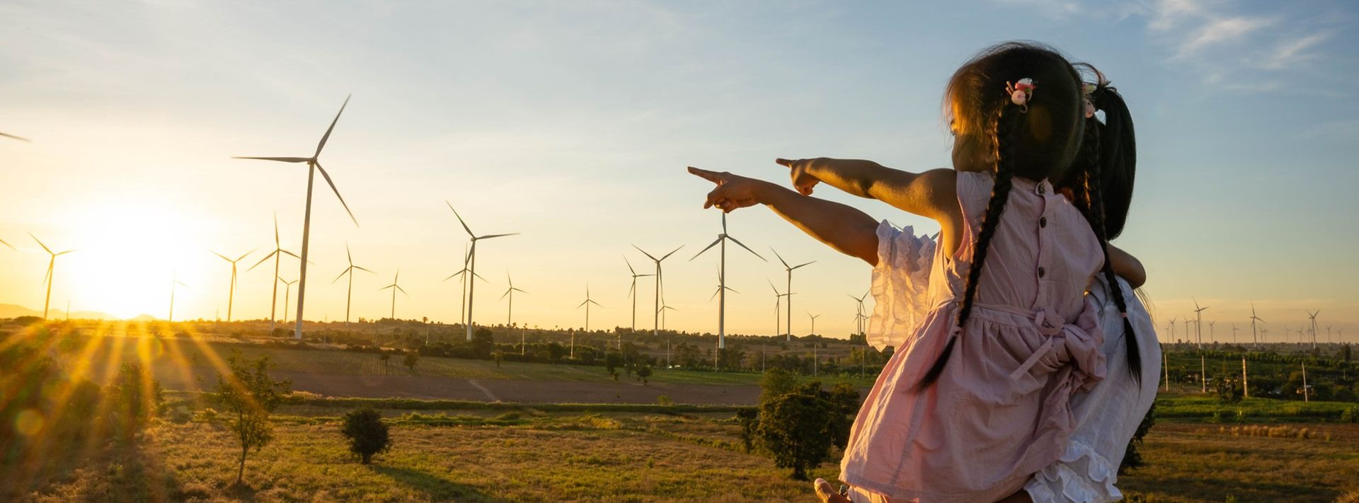 Mutter mit Tochter auf dem Arm schauen zu einem Windpark bei Sonnenaufgang
