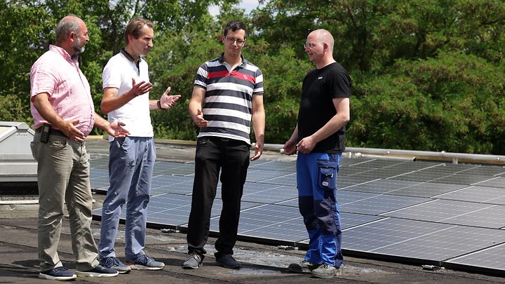 Vier Männer stehen auf einem Dach mit Solarpaneelen und diskutieren.