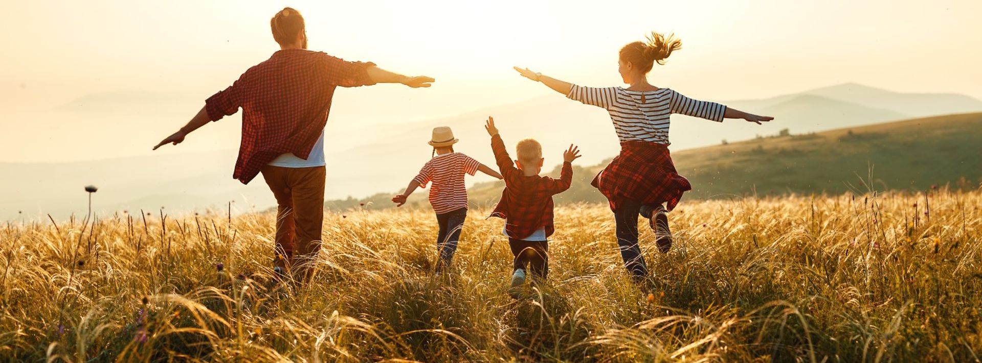 © www.istockphoto.com/evgenyatamanenko Junge Familie rennt auf Feld der untergehenden Sonne entgegen
