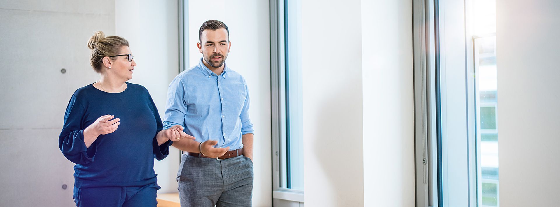© Mainova/AndreFormer Frau und Mann laufen vor Fensterwand und sprechen miteinander