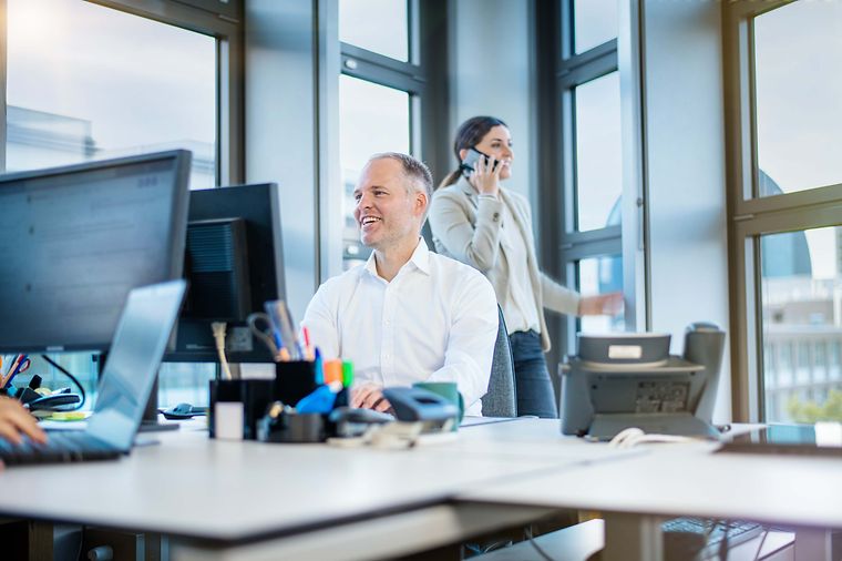 © Mainova/AndreFormer Ein Mitarbeiter sitzt am Tisch und lacht auf seinen Monitor