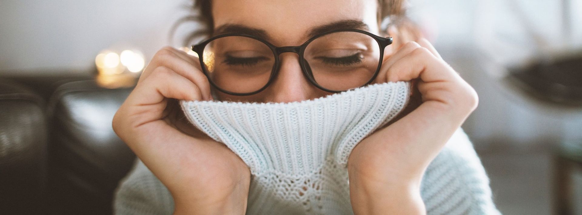 Frau mit Brille zieht weißen Rollkragen über Mund und Nase