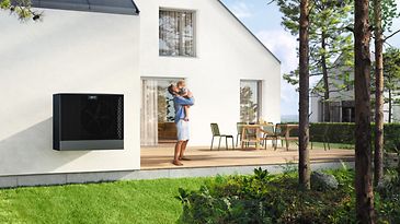 Mann und Kind spielen auf der Terrasse ihres Einfamilienhauses, das mit einer Wärmepumpe ausgestattet ist.